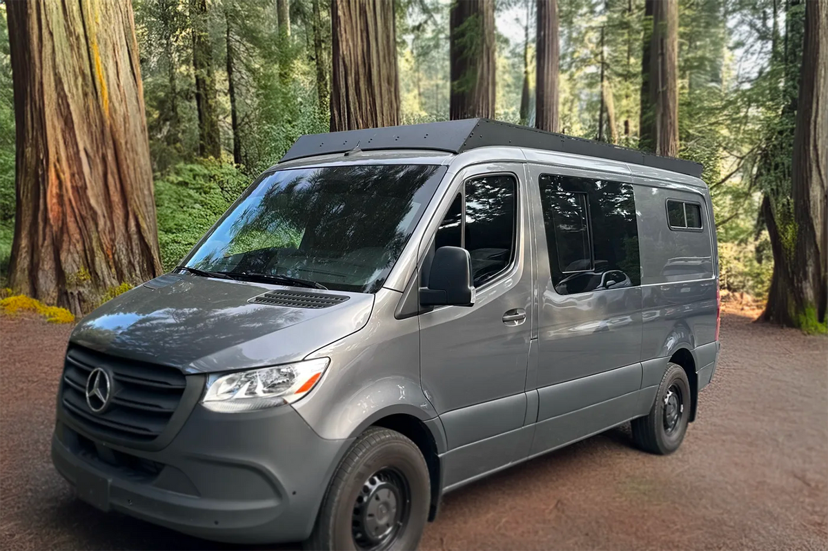 A gray Mercedes-Benz Sprinter Low Standard Roof van parked on a dirt path surrounded by tall redwood trees in a forest with orion van gear roof rack